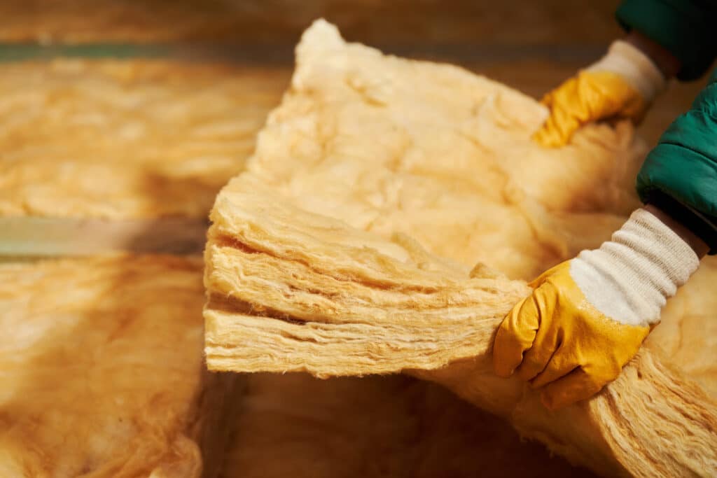 Isolation Laine de Verre : Pose d'Isolant Thermique Ouvrier portant des gants jaunes manipulant des épaisseurs de laine de verre isolante de couleur ambre.