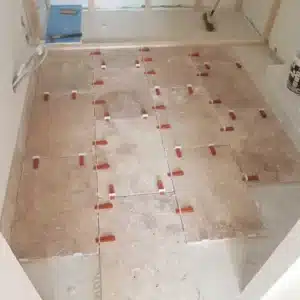 Pose de carrelage en travertin beige avec des croisillons rouges de nivellement assurant des joints uniformes sur un sol en construction.